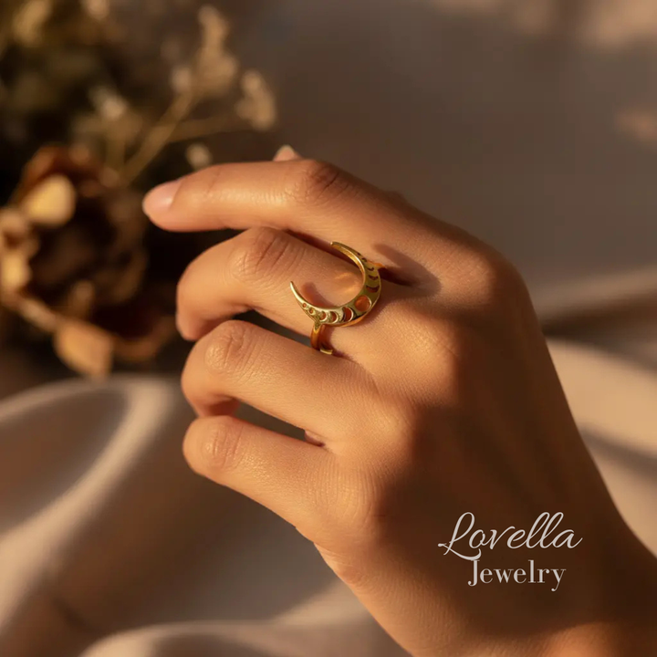Hand wearing a gold ring with a blurred natural background, featuring Lovella Jewelry branding.
