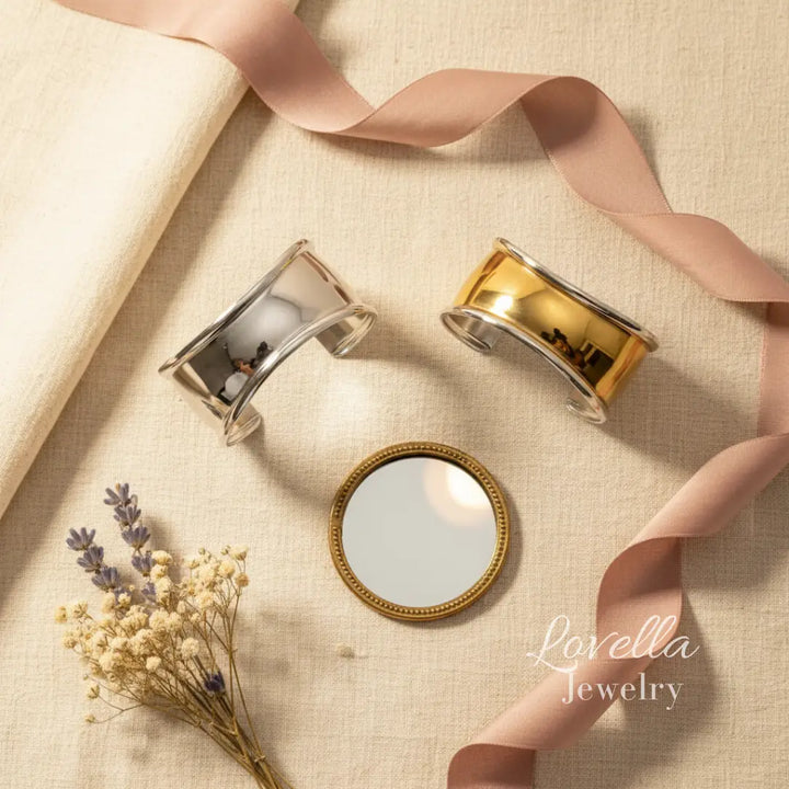 Two gold bracelets and a small round mirror on a beige fabric background with 'Lovella Jewelry' branding.