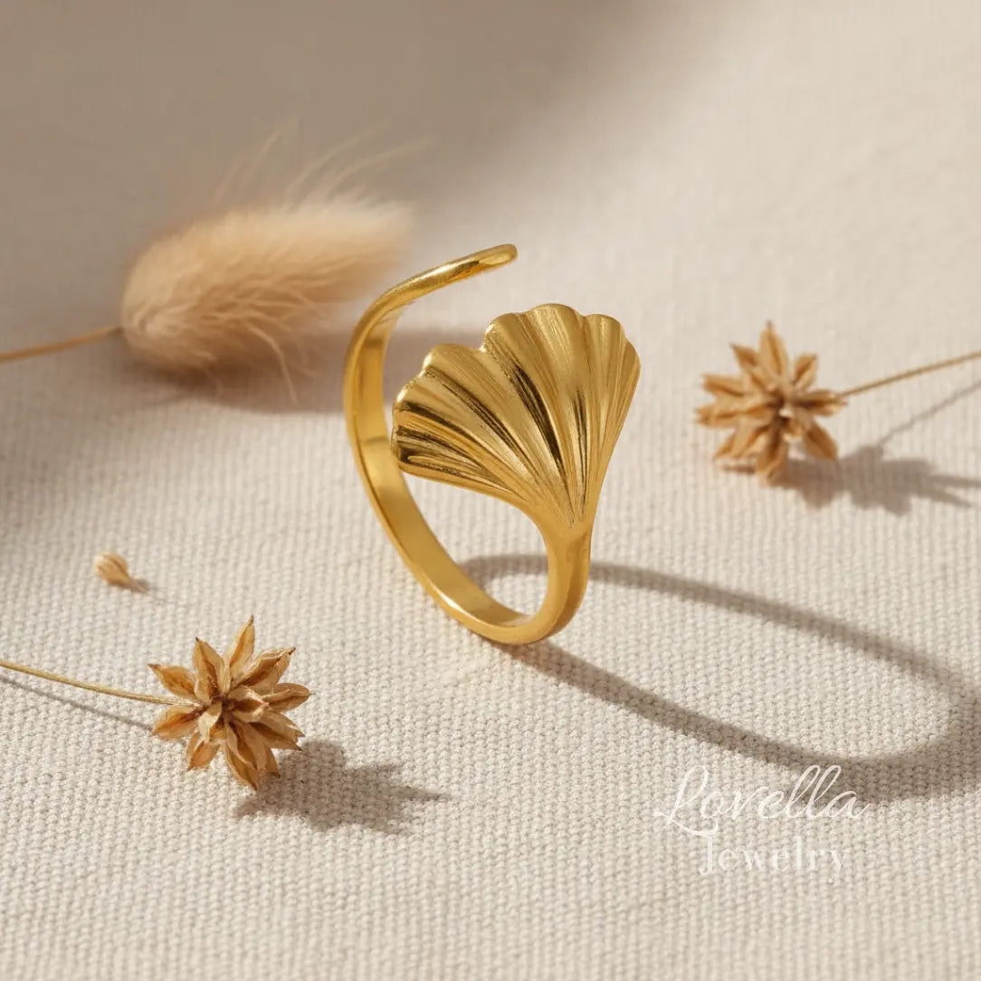 Gold leaf-shaped ring on a textured beige surface with dried flowers.