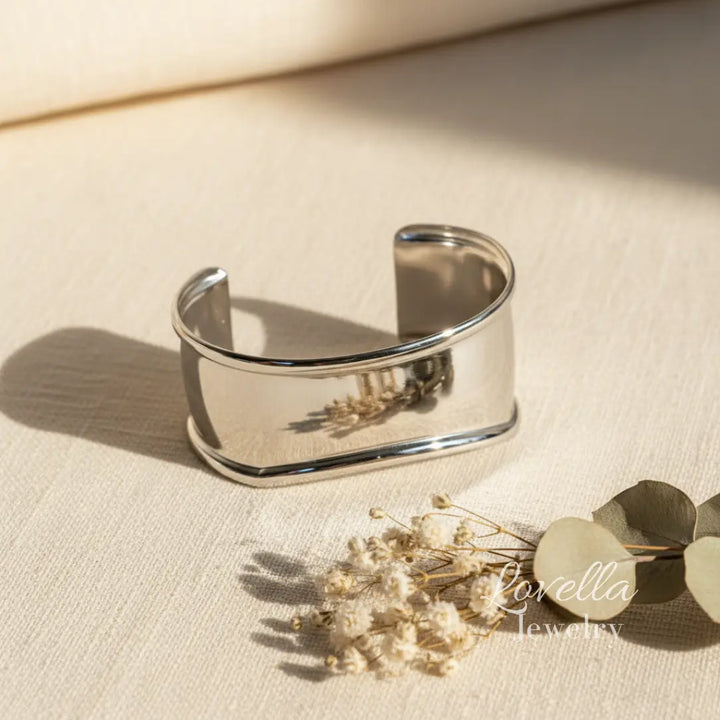 Silver cuff bracelet on a beige fabric background with Lovella Jewelry branding.