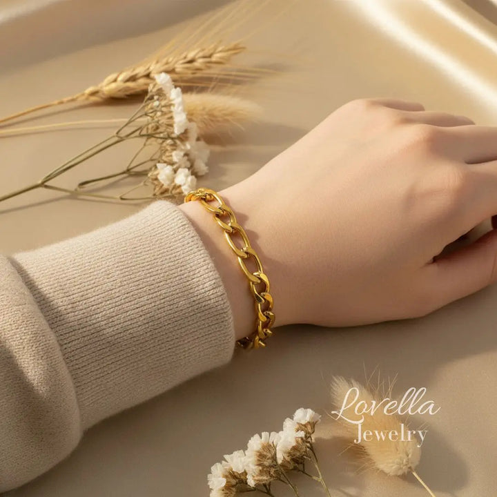 Gold chain bracelet on a wrist with dried flowers on a beige background, featuring Lovella Jewelry.