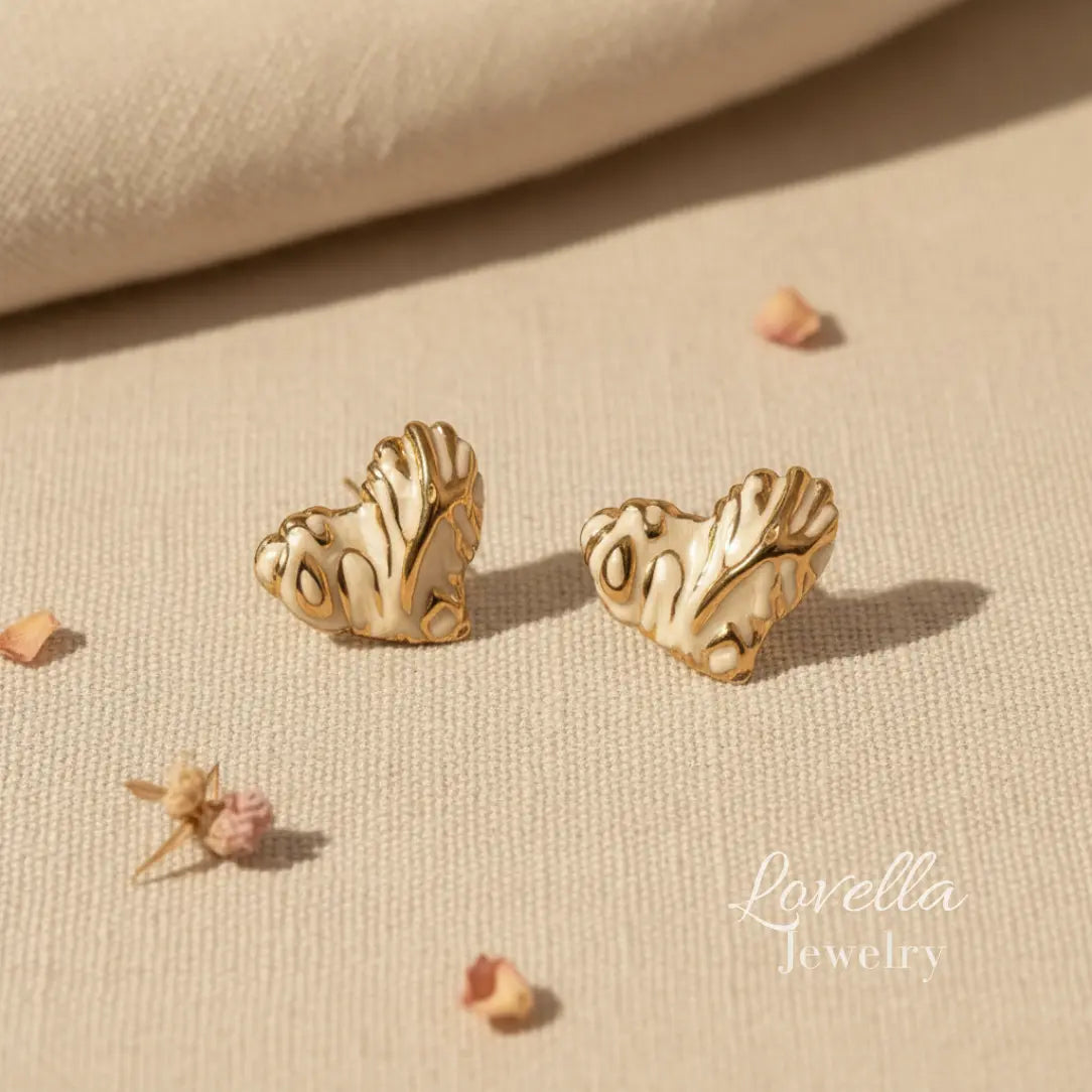 Gold heart-shaped earrings on a beige fabric background with 'Lovella Jewelry' branding.