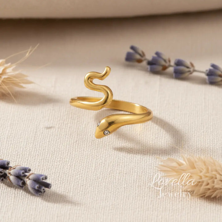 Gold snake-shaped ring on a beige fabric background with lavender flowers.