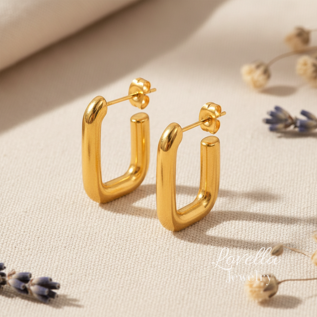 Gold hoop earrings on a beige surface with dried flowers.