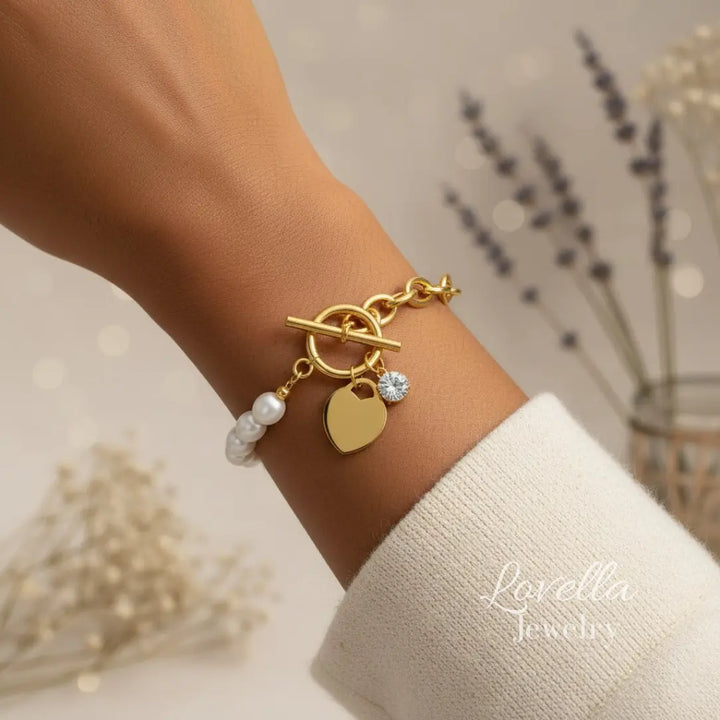 Gold bracelet with heart charm and pearl beads on a wrist, brand 'Lavella' visible.