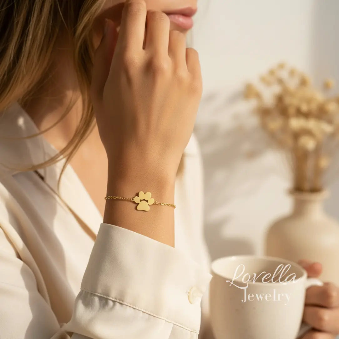 Woman wearing a gold bracelet with a blurred background featuring a vase and flowers.