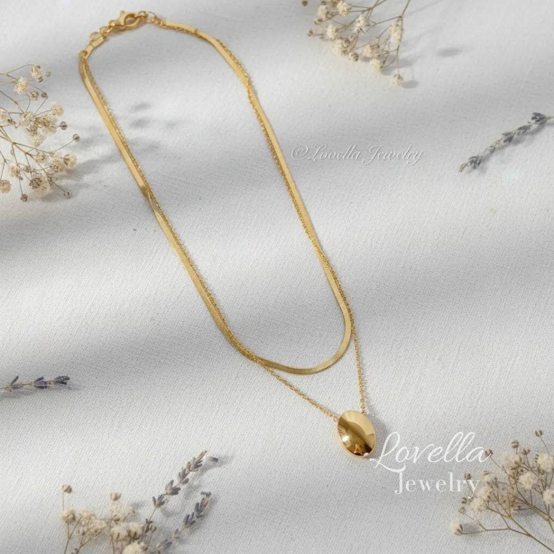 Gold necklace with a pendant on a light background with dried flowers.