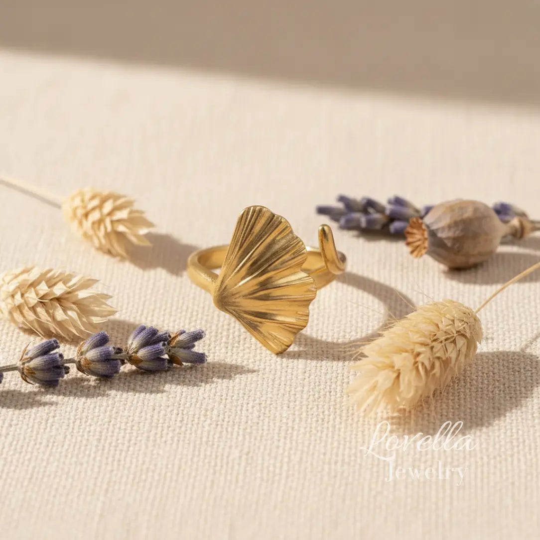 Gold ring with shell design on a beige surface with dried flowers and plants.