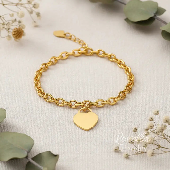 Gold bracelet with a heart-shaped tag on a light background with greenery