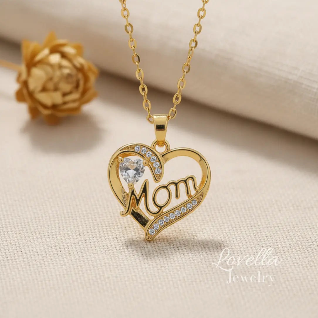 Gold-tone stainless steel "Mom" heart necklace with zirconia stones and a large clear center stone, displayed on a delicate chain.