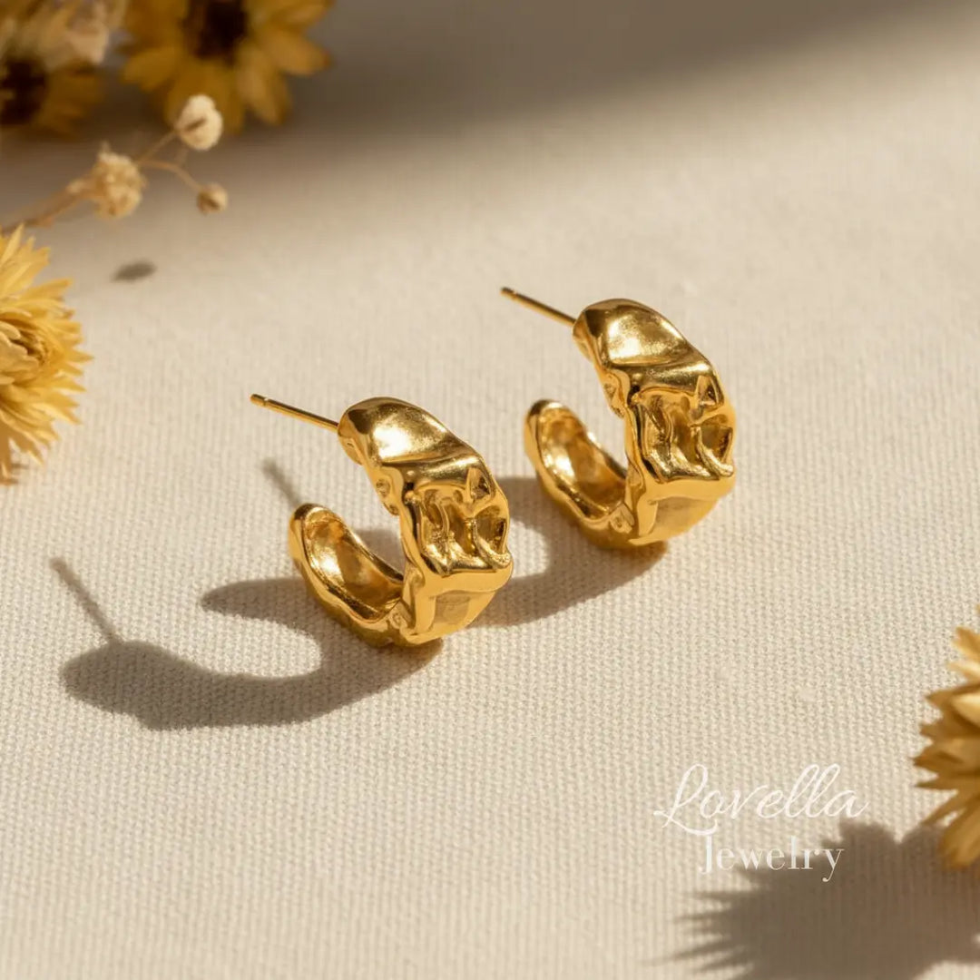 Gold hoop earrings on a beige surface with dried flowers
