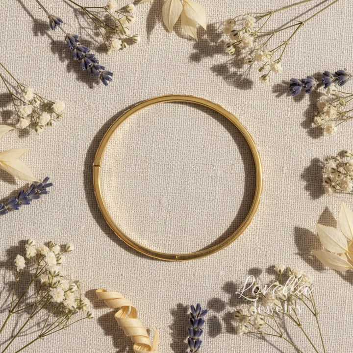 Gold bracelet on a textured surface with dried flowers