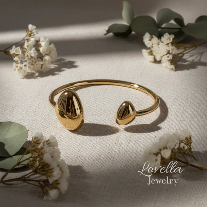 Gold bracelet with teardrop-shaped ends on a light fabric background with flowers and leaves.