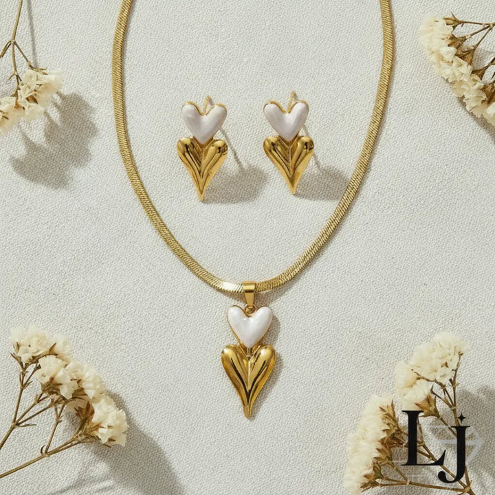 Gold necklace and earrings with heart-shaped white pendants on a light background with flowers.