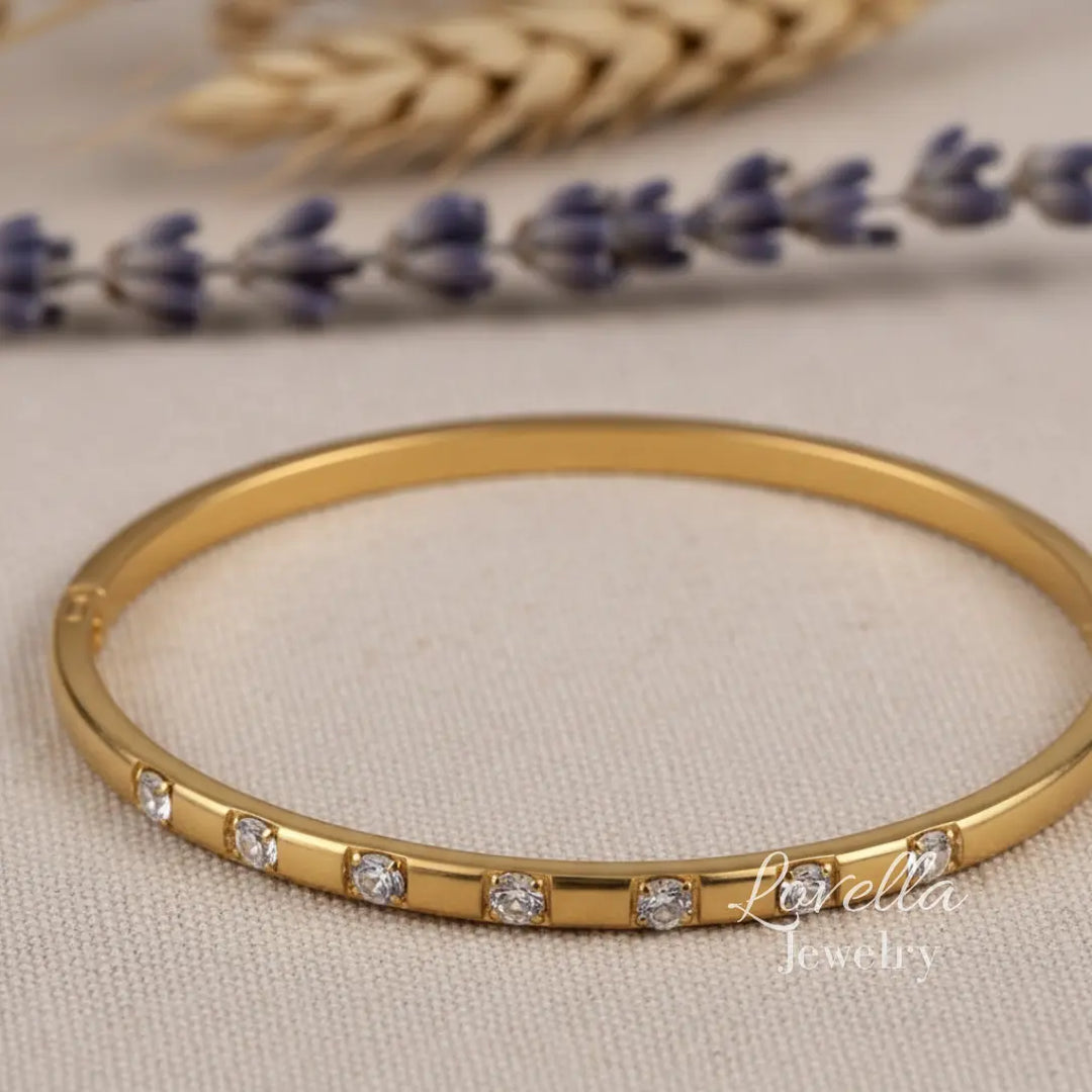 Gold bracelet with diamonds on a beige fabric background with lavender and wheat.