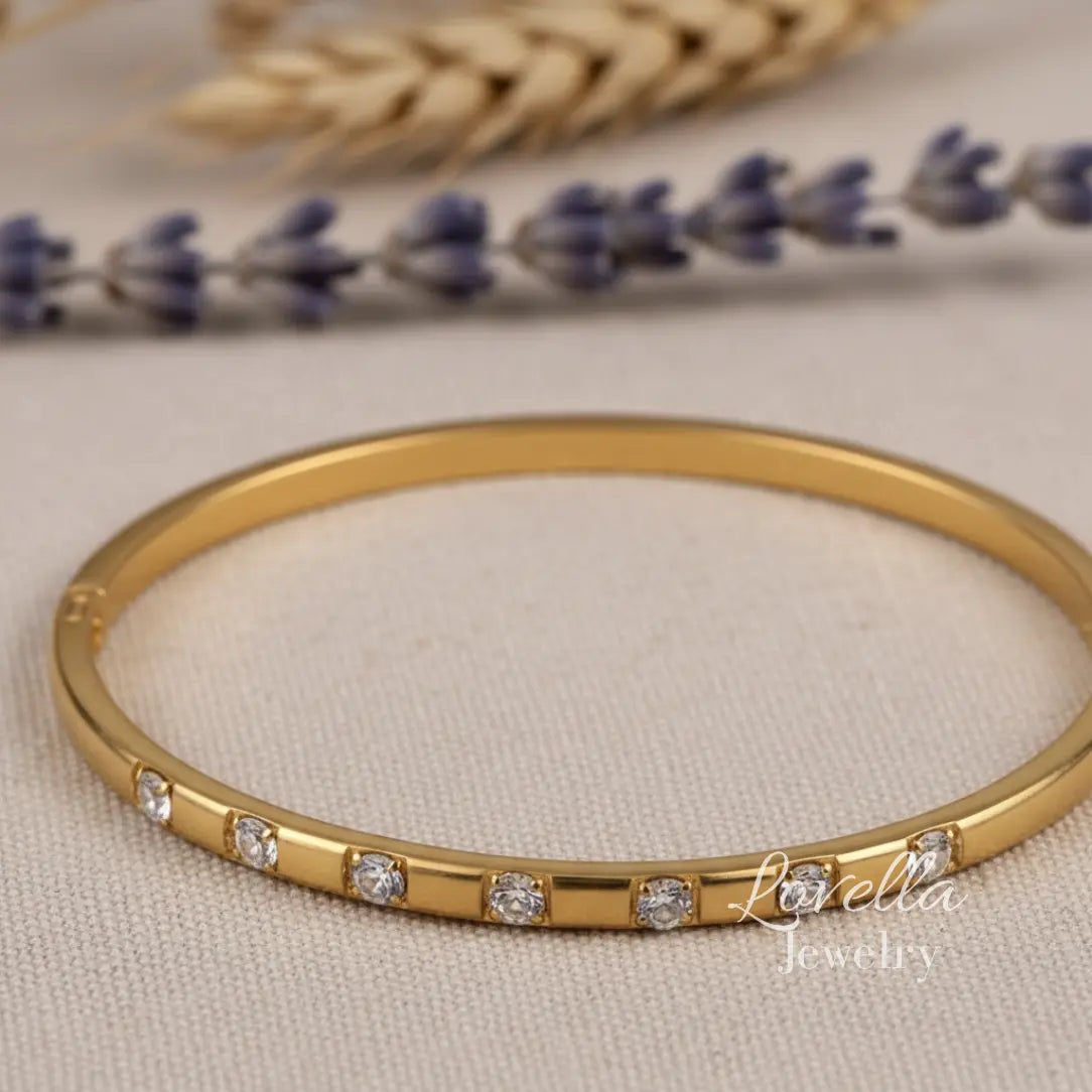 Gold bracelet with diamonds on a beige fabric background with lavender and wheat.