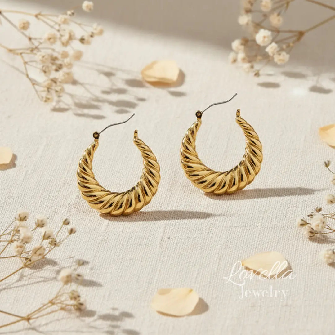 Gold hoop earrings on a light fabric background with dried flowers.