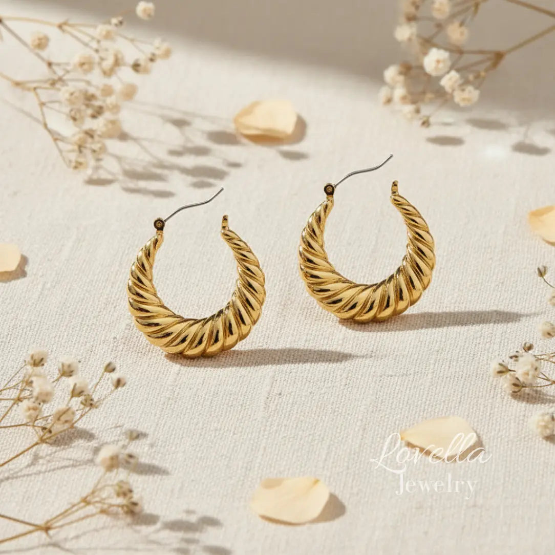 Gold hoop earrings on a light fabric background with dried flowers.