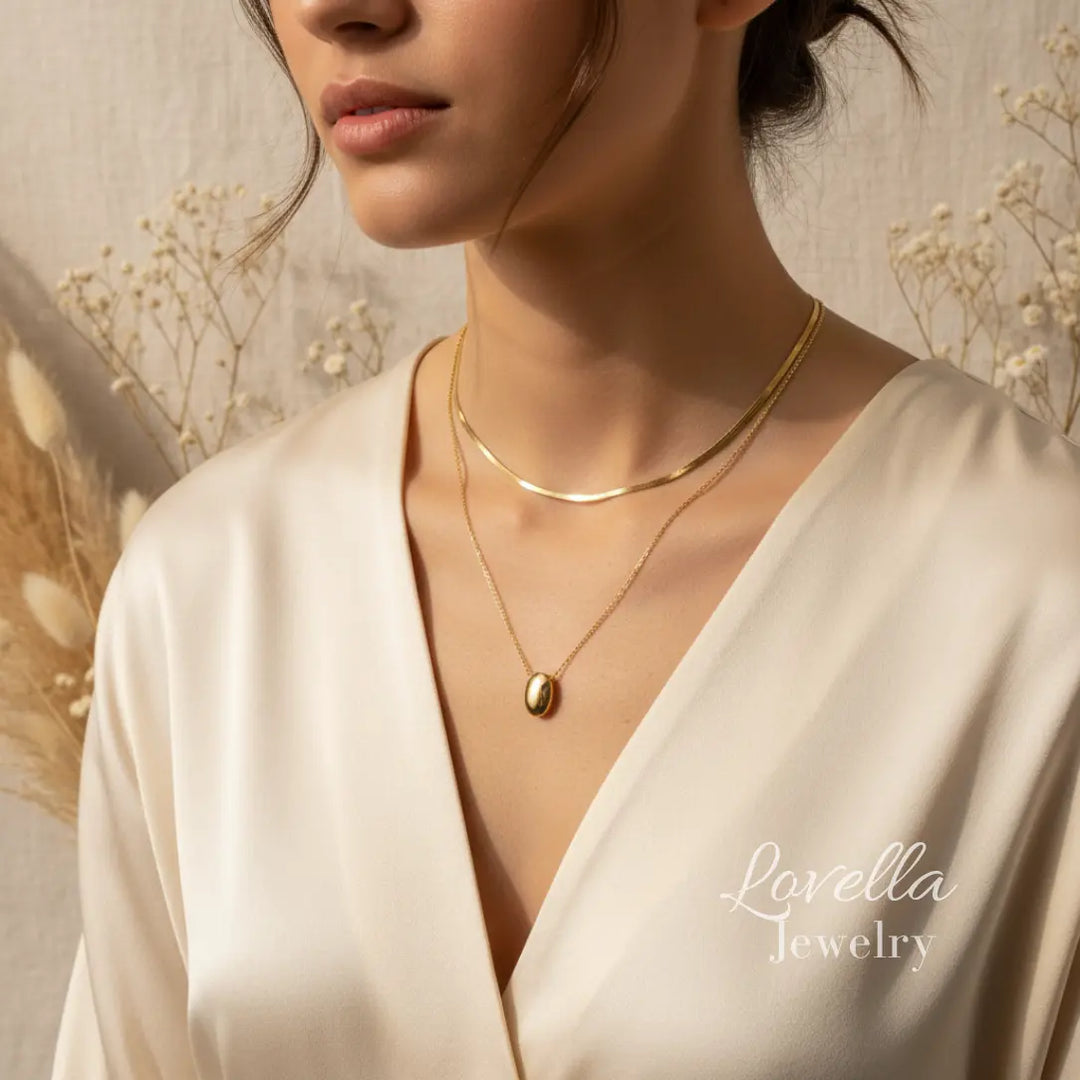 Woman wearing a gold necklace with a gold pendant, set against a neutral background with 'Lovella Jewelry' branding.