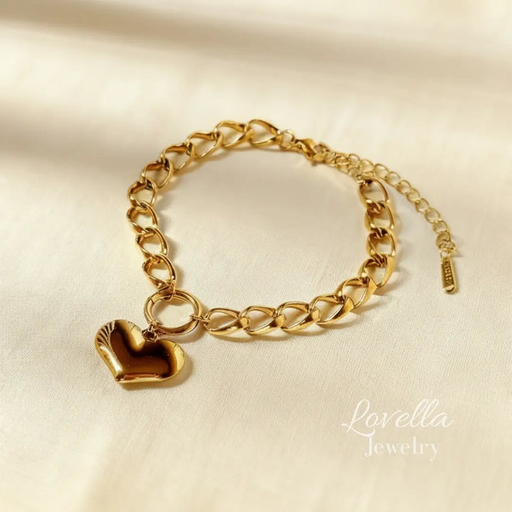 Gold chain bracelet with a heart charm on a beige background, branded 'Lovella Jewelry'.