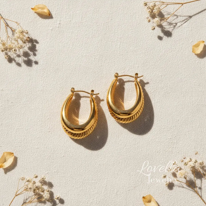 Gold hoop earrings on a light background with dried flowers.