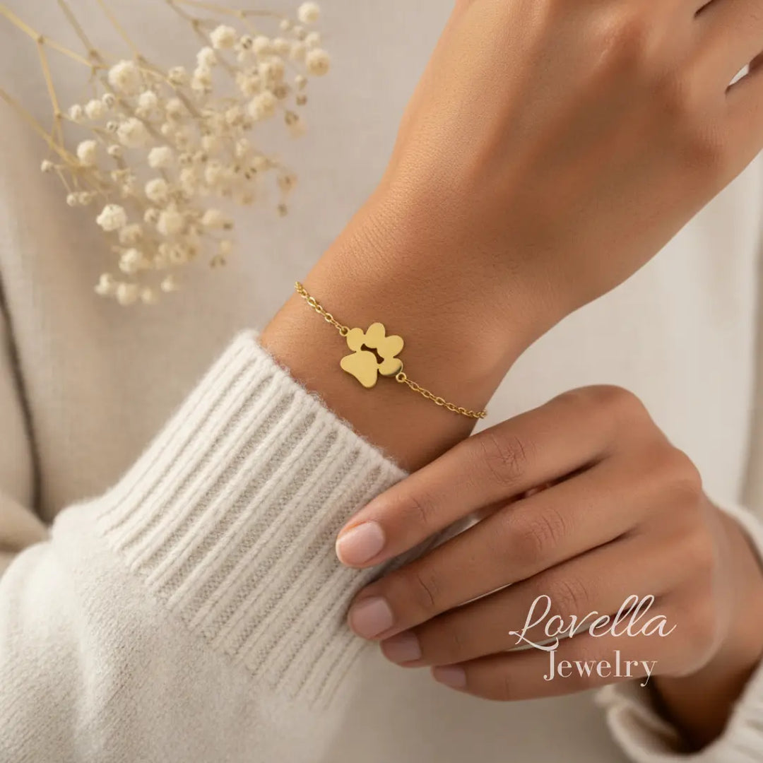 Gold paw print bracelet on a wrist with a neutral background and 'Lovella Jewelry' branding.