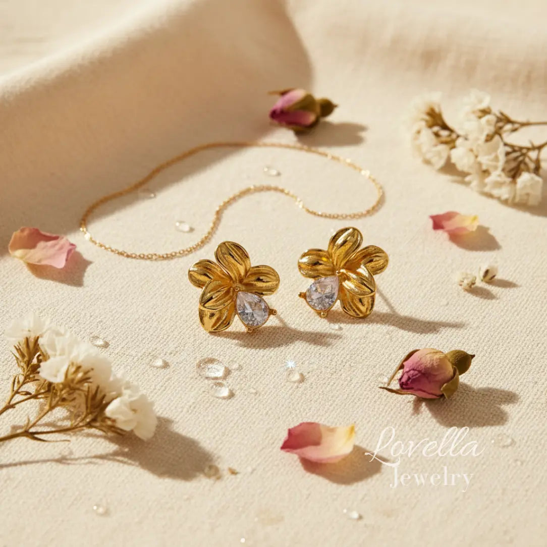 Gold floral earrings with clear stones on a beige surface with dried flowers.