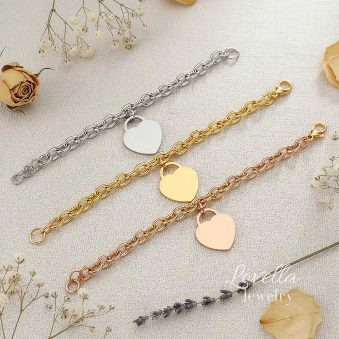 Three heart-shaped bracelet charms on gold, silver, and rose gold chains with dried flowers in the background.