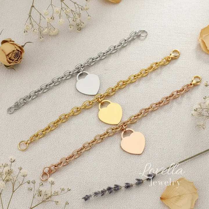 Three heart-shaped bracelet charms on gold, silver, and rose gold chains with dried flowers in the background.