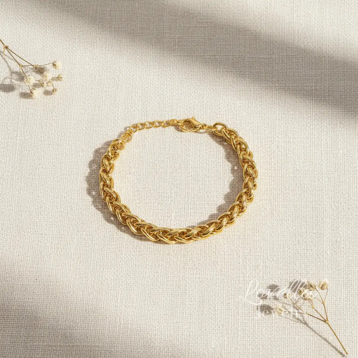Gold chain bracelet on a light beige fabric background with dried flowers.
