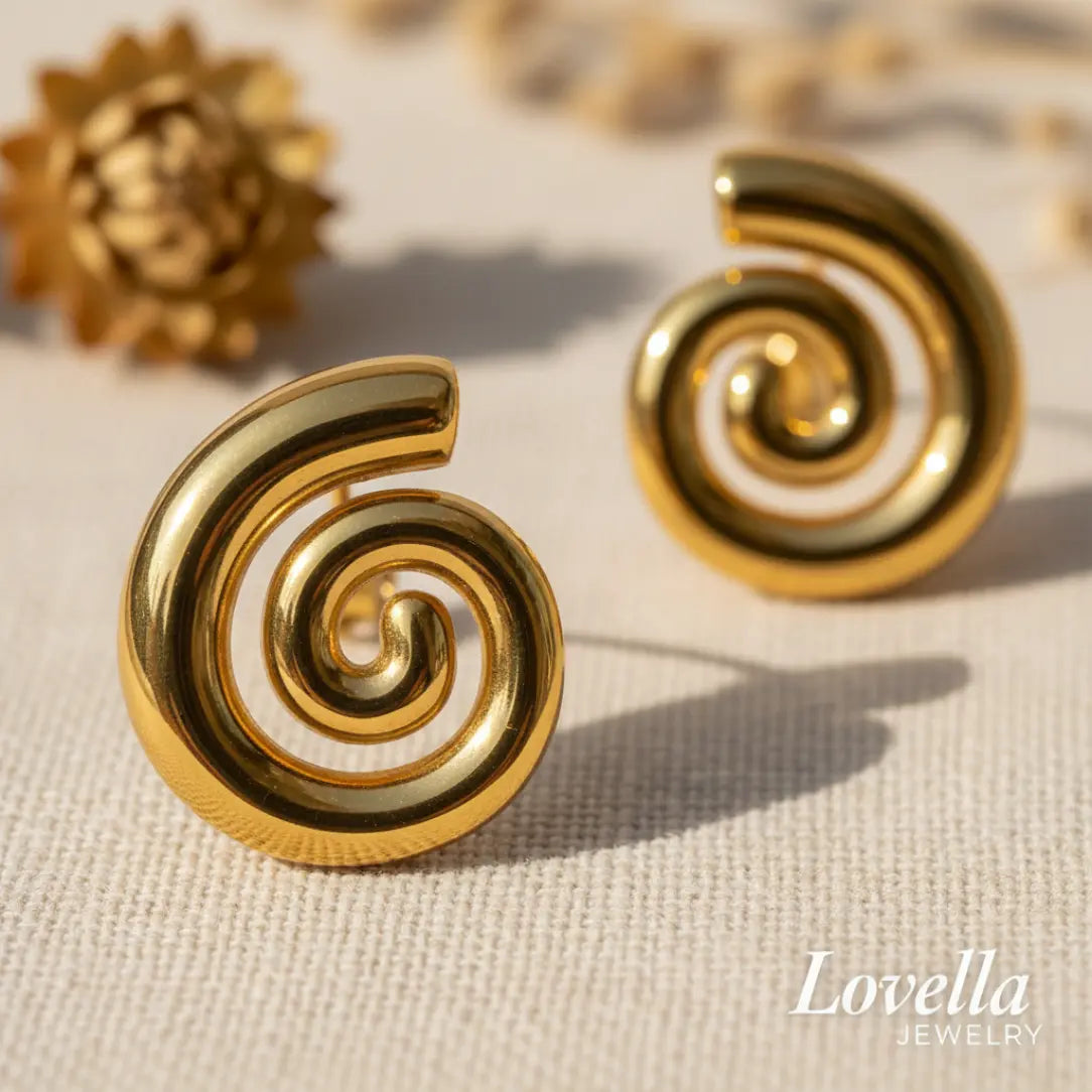 Gold spiral earrings on a textured beige surface with 'Lovella Jewelry' branding.