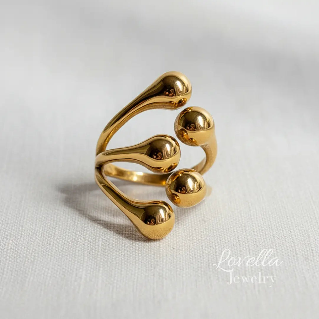 Close-up of a gold-tone stainless steel bubble ring with multiple rounded bead details on a neutral fabric background.