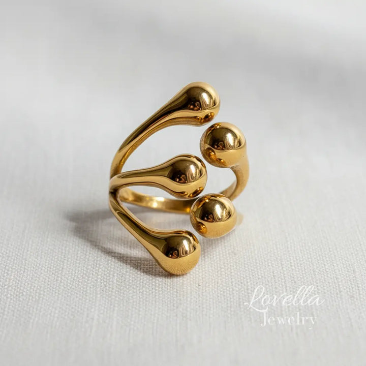 Close-up of a gold-tone stainless steel bubble ring with multiple rounded bead details on a neutral fabric background.