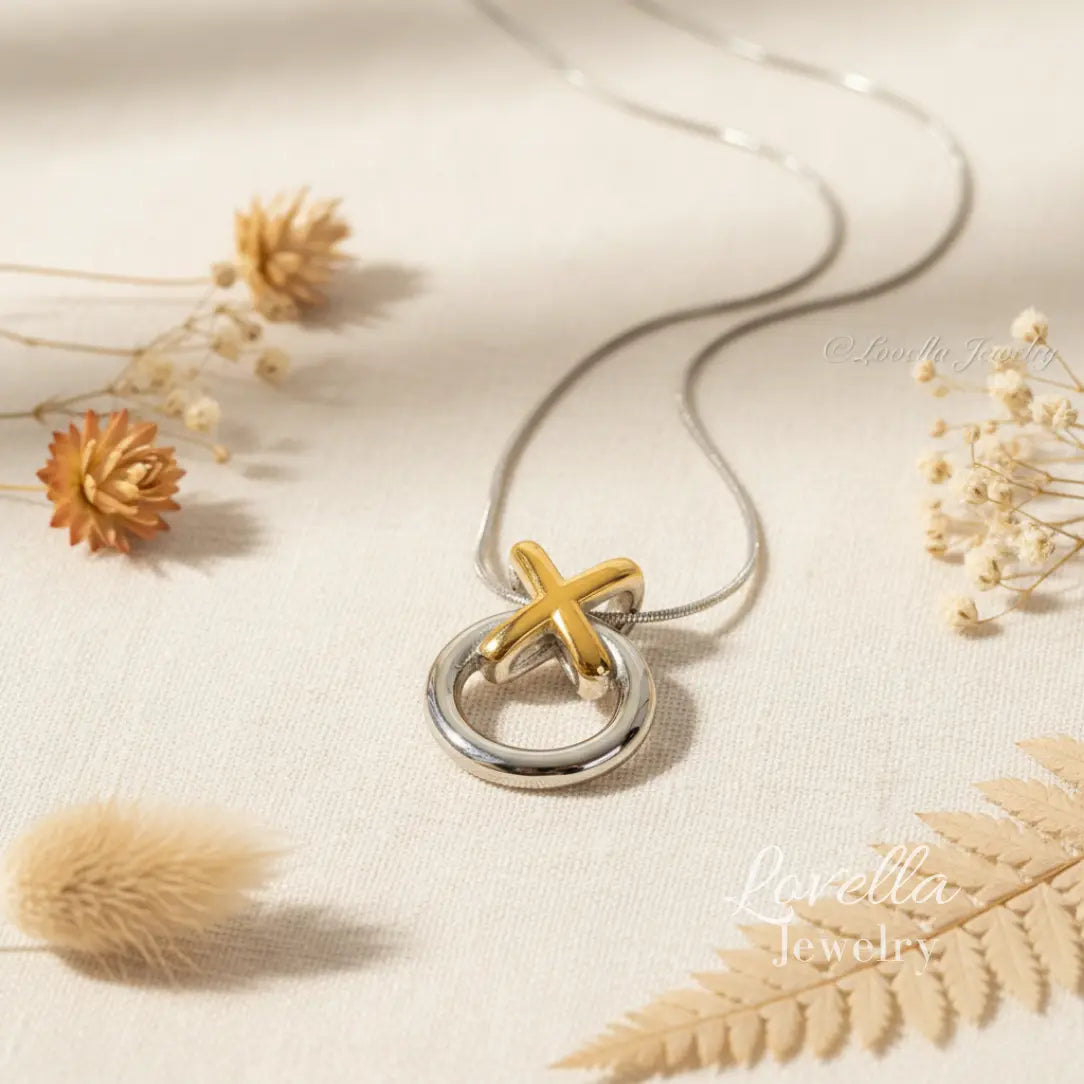 Necklace with a gold and silver pendant on a beige background with dried flowers.