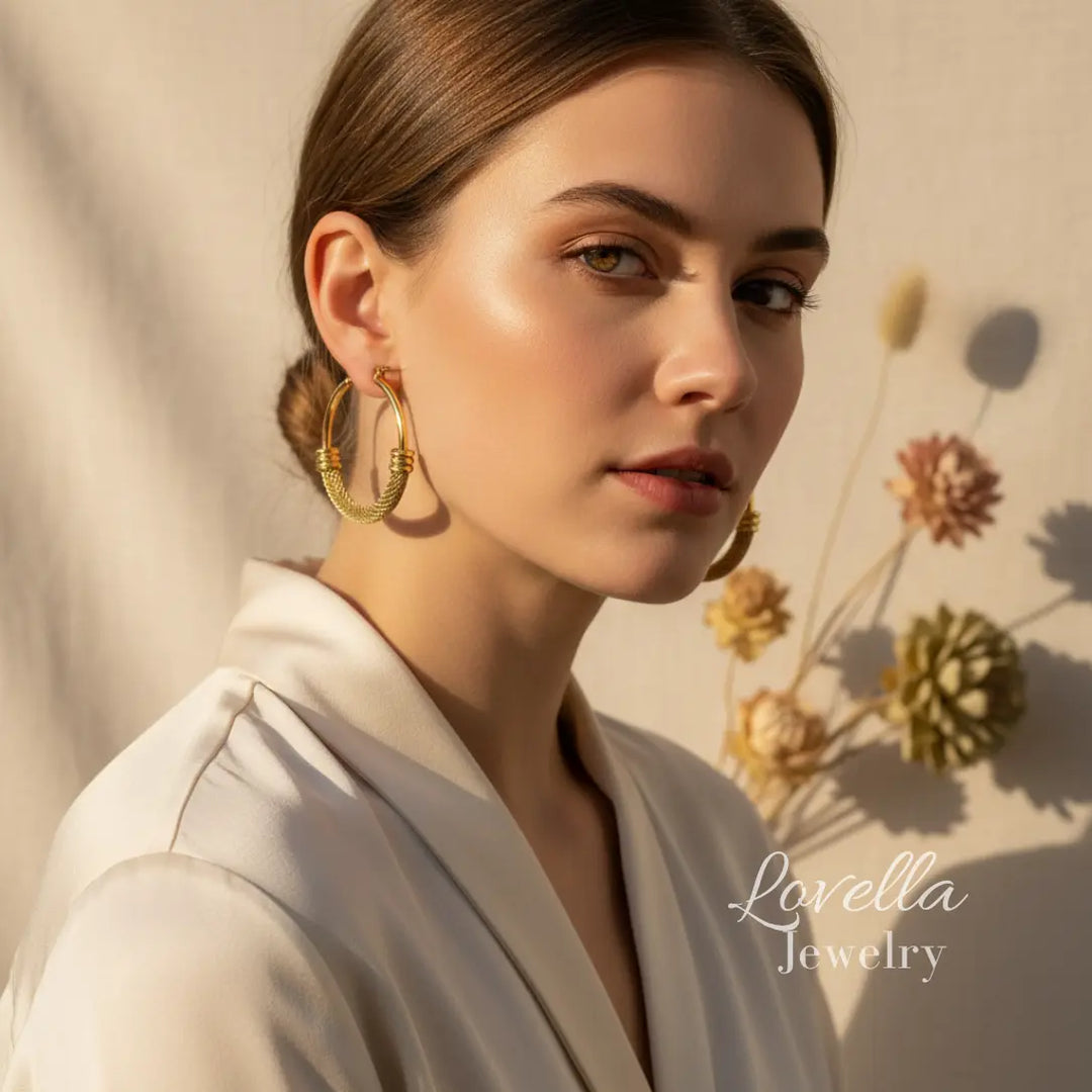 Woman wearing gold hoop earrings with a neutral background and 'Lovella Jewelry' branding.