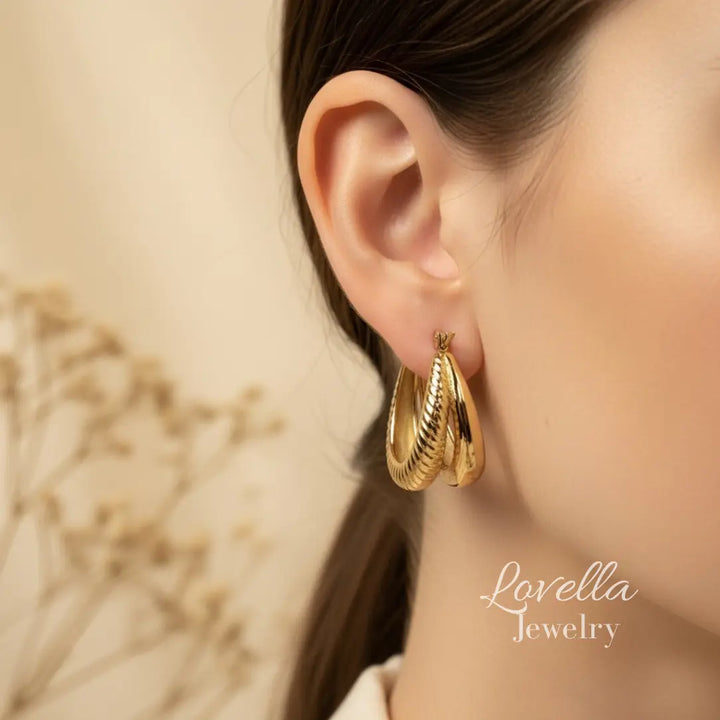 Gold hoop earrings worn by a person with a blurred background, featuring Lovella Jewelry branding.