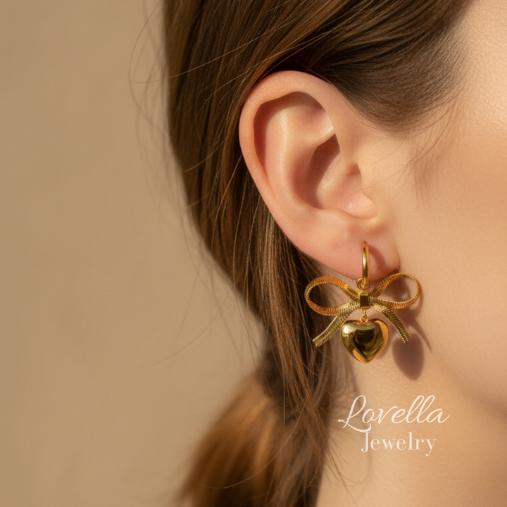 Gold bow-shaped earring worn by a person with a neutral background, featuring Lovella Jewelry branding.