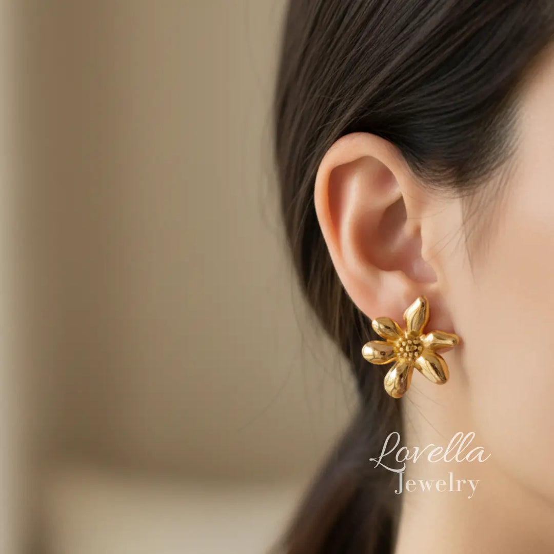 Woman modelong Gold flower stud earrings on cream linen background with eucalyptus shadows and Lovella Jewelry logo