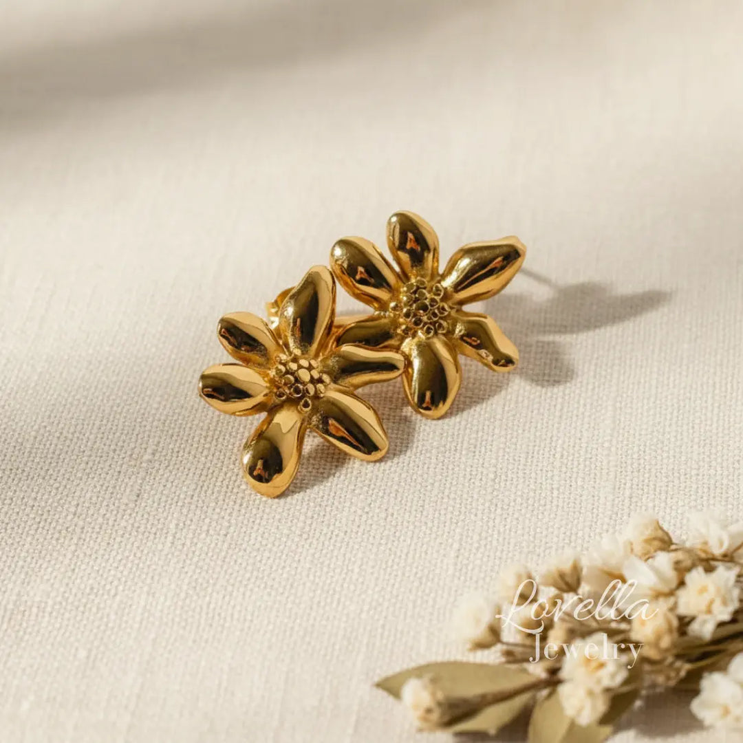 Gold flower stud earrings on cream linen background with eucalyptus shadows and Lovella Jewelry logo