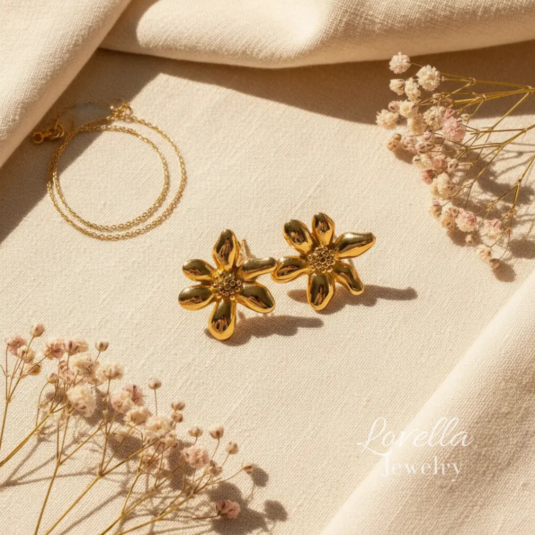 Gold flower stud earrings on cream linen background with eucalyptus shadows and Lovella Jewelry logo