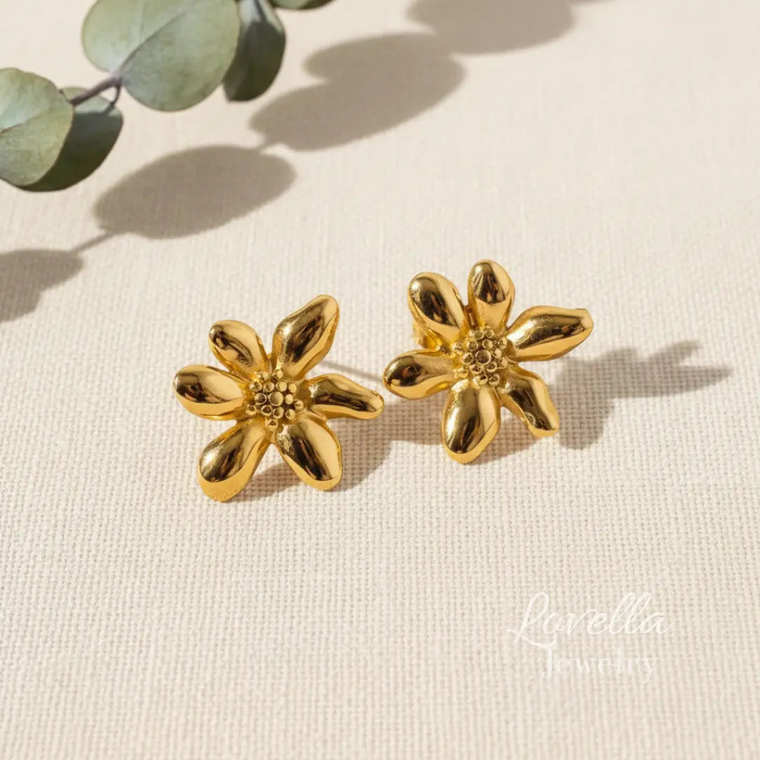 Gold flower stud earrings on cream linen background with eucalyptus shadows and Lovella Jewelry logo