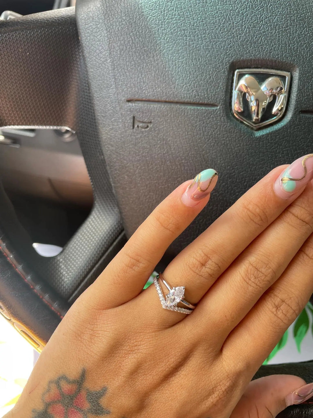 Hand wearing a diamond ring with a car steering wheel in the background
