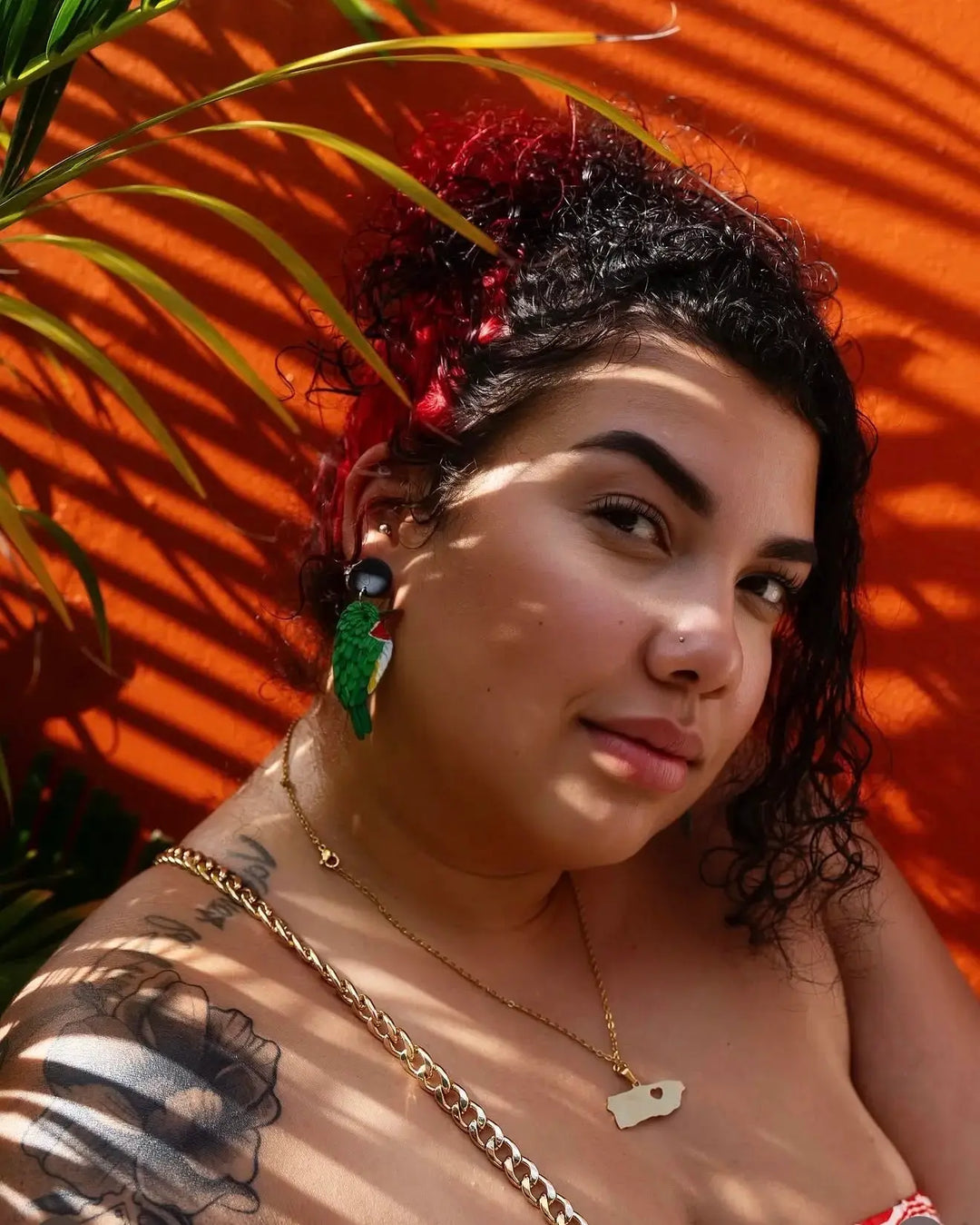 Woman with tattoos and jewelry against an orange wall